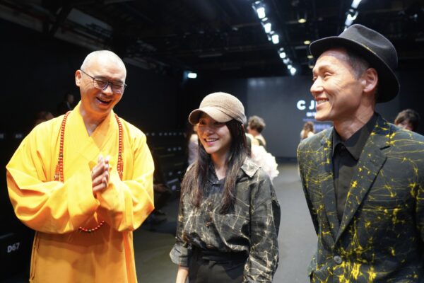 C JEAN 於文化部主辦26AW 臺北時裝週開幕秀現場,圖中合影除模特兒外,唯一女性為品牌設計師簡君媛;首秀焦點模特兒手持之經書, 國立故宮博物院與僧伽林文化出版有限公司合作之國寶復刻文創「普門品」。圖/楠西萬佛寺