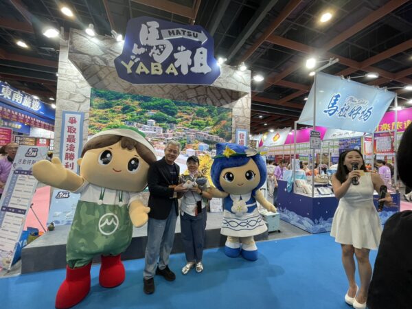 2026台北國際夏季旅展馬祖主題館舉辦互動問答活動,民眾熱情參與並成功答題,開心獲得精美馬祖特色贈品,在吉祥物陪伴下合影留念,現場氣氛熱絡,吸引不少民眾駐足參與。(朱立君攝)