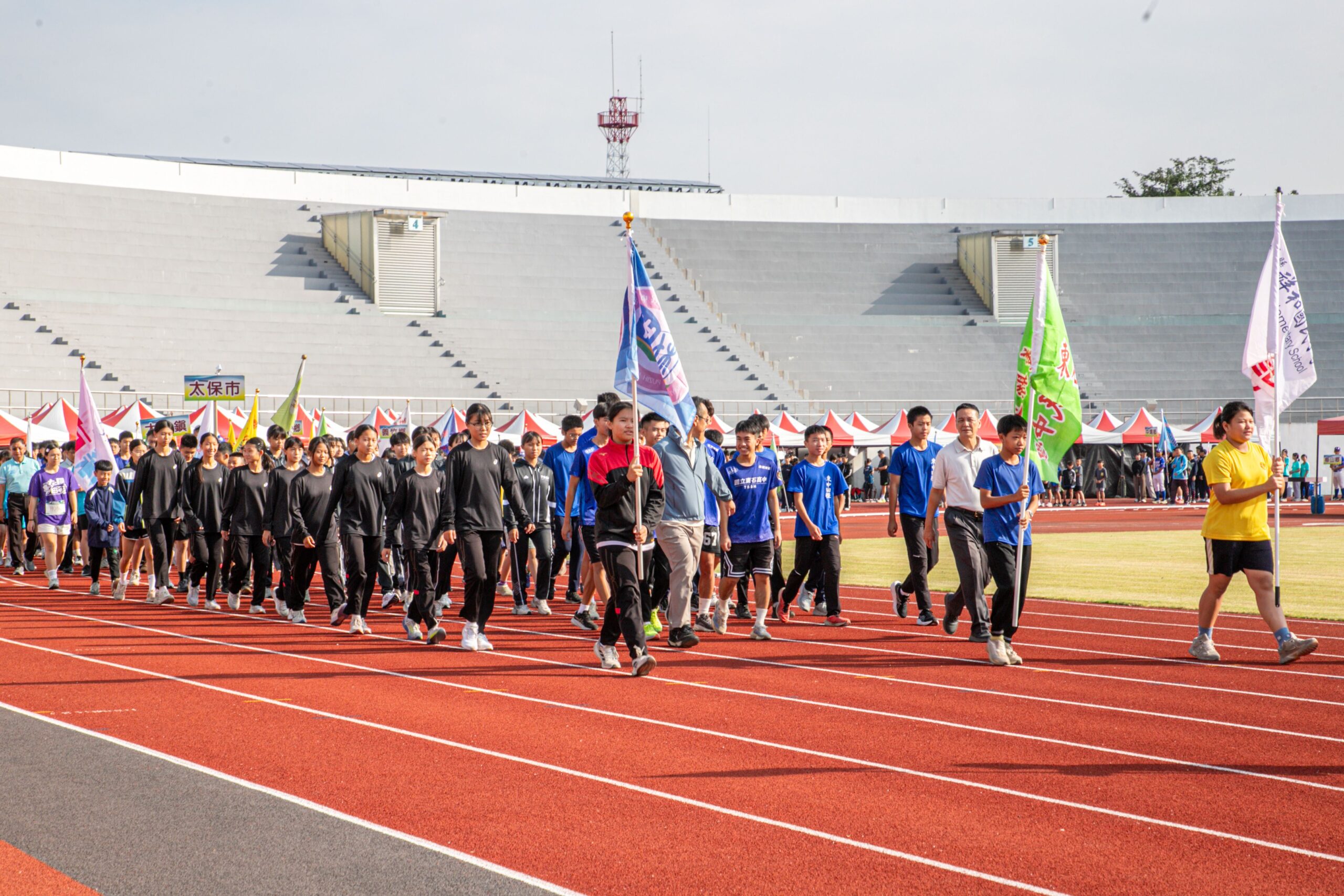 嘉義縣115年中小學聯合運動會開幕，各校選手在校旗引領下依序進場，展現昂揚朝氣，迎接競技挑戰。（圖／嘉義縣政府提供）